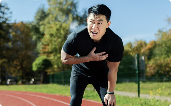 An Asian man on a running track, clutching his chest with a pained expression.