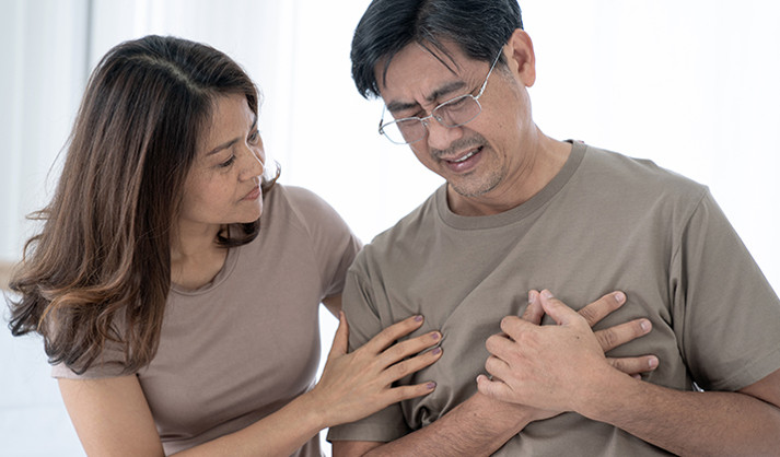 A woman comforts a man clutching his chest, distressed from a possible heart attack.